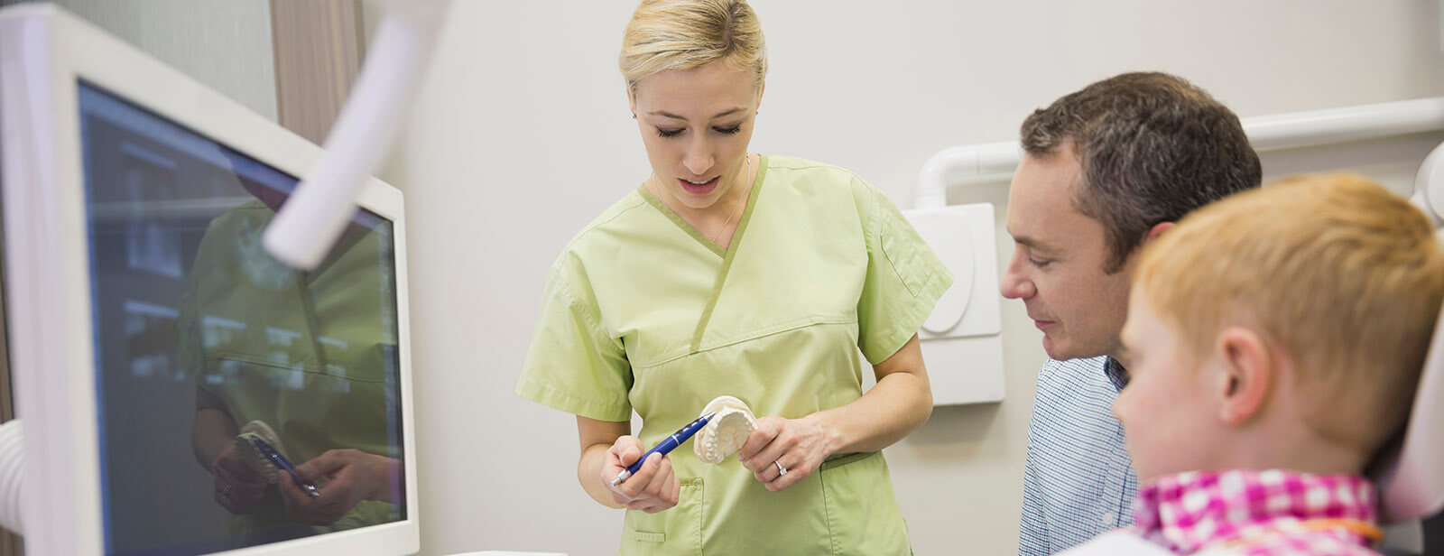 hygienist-communicative-training dental hygienist showing model of mouth to man and boy