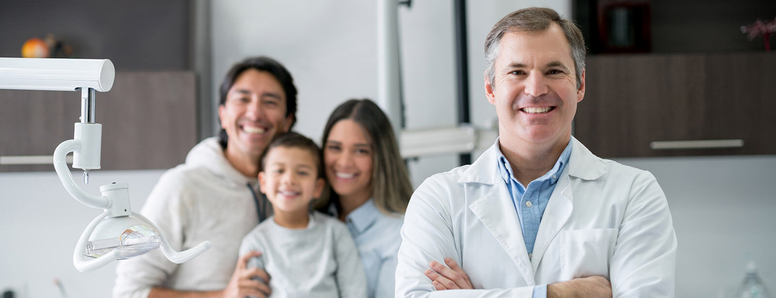 retaining-dentists Portrait of a dentist at the office looking very happy with a family at the background and smiling - healthcare and medicine concepts